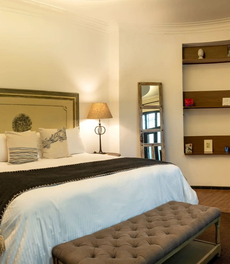 Bed with a painted-frame upholstered headboard, a tufted bench and timber niches on the curved wall
