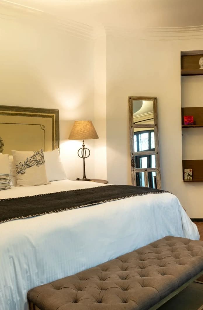 Bed with a painted-frame upholstered headboard, a tufted bench and timber niches on the curved wall