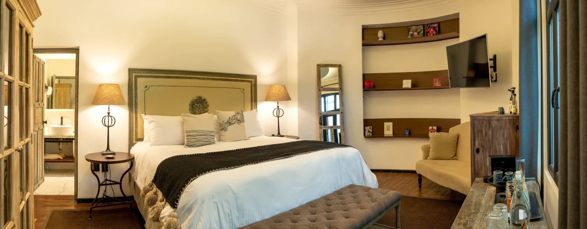Bed with a painted-frame upholstered headboard, a tufted bench and timber niches on the curved wall