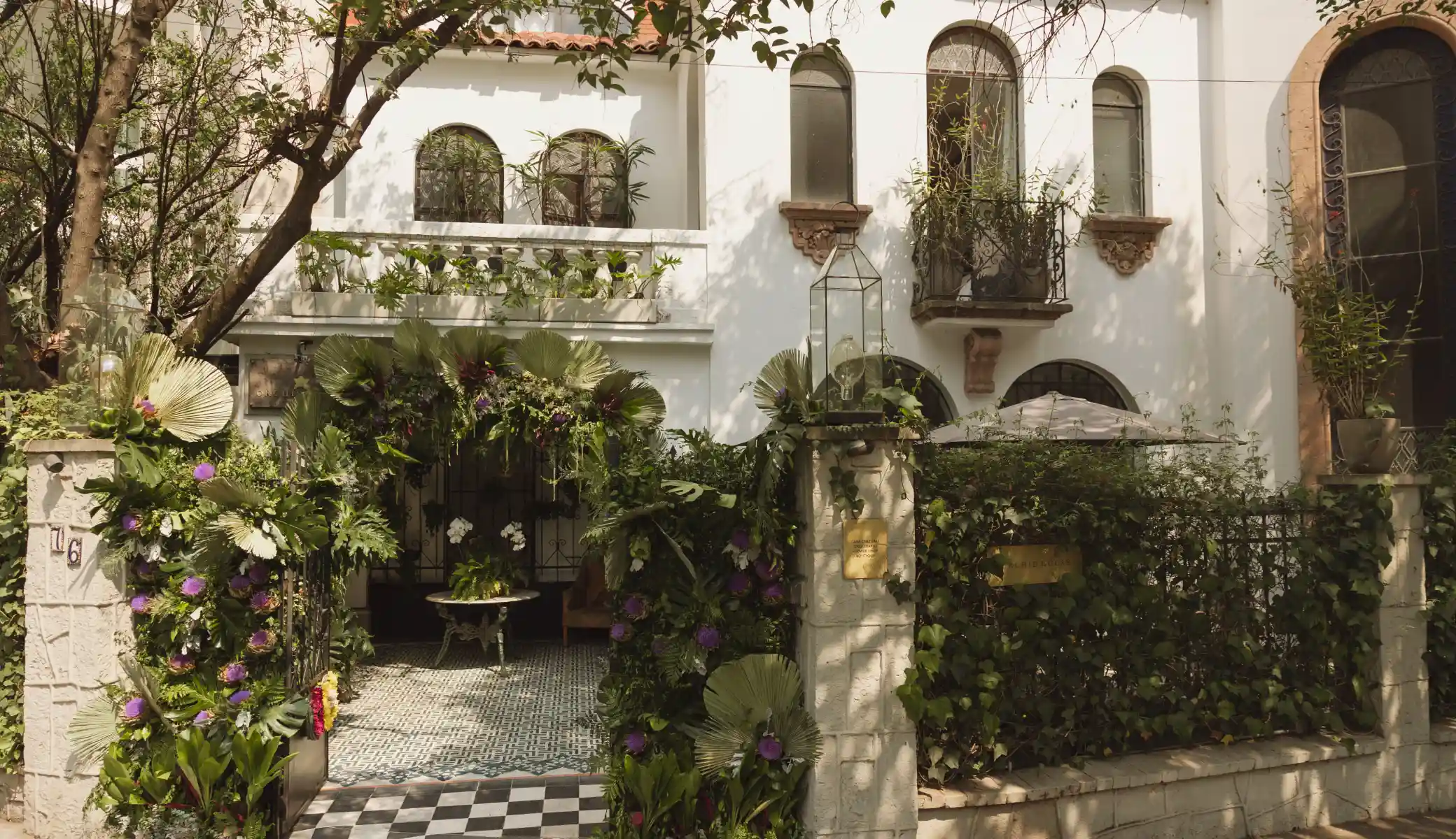 The entrance to Orchid House Mexico City from the street, with the arch of flowers and palm leaves over the gate and the chequered floor of the entrance