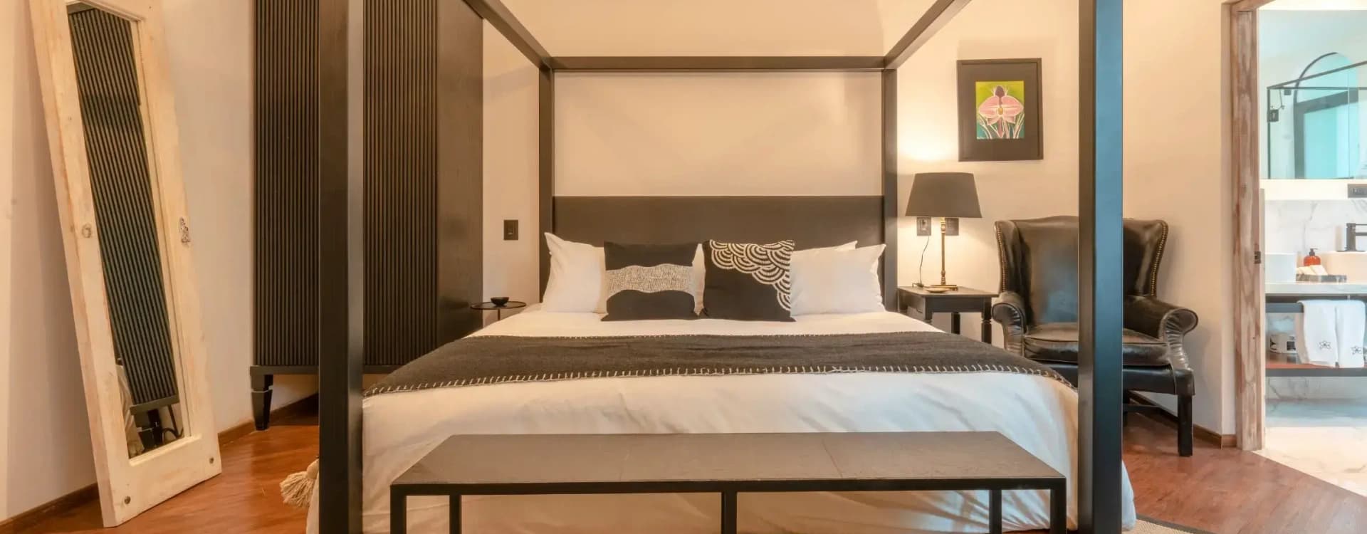 Dark-timber four-poster bed with a wrought-iron bench and a leather armchair