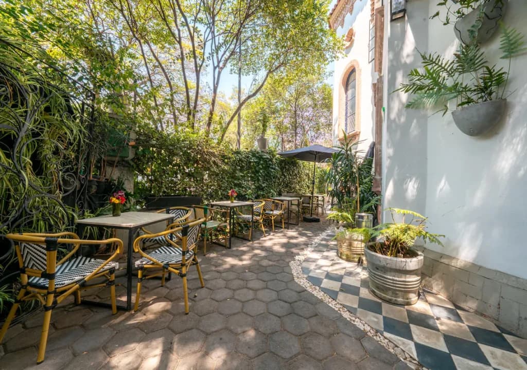 The garden terrace of the Polanco house, with bistro tables under the trees and the chequered floor of the hallway