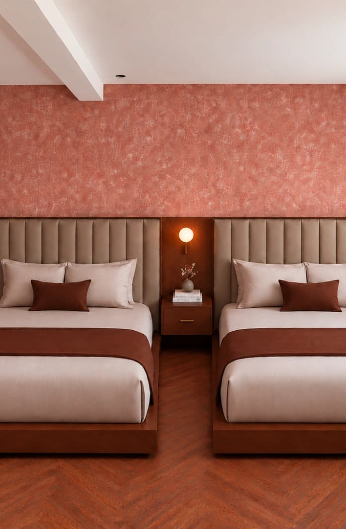 Two beds with channel-tufted headboards beneath a coral textured wall, a lit nightstand between them