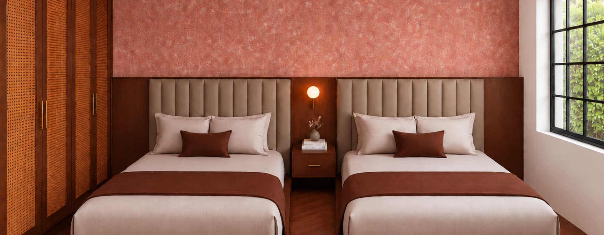 Two beds with channel-tufted headboards beneath a coral textured wall, a lit nightstand between them