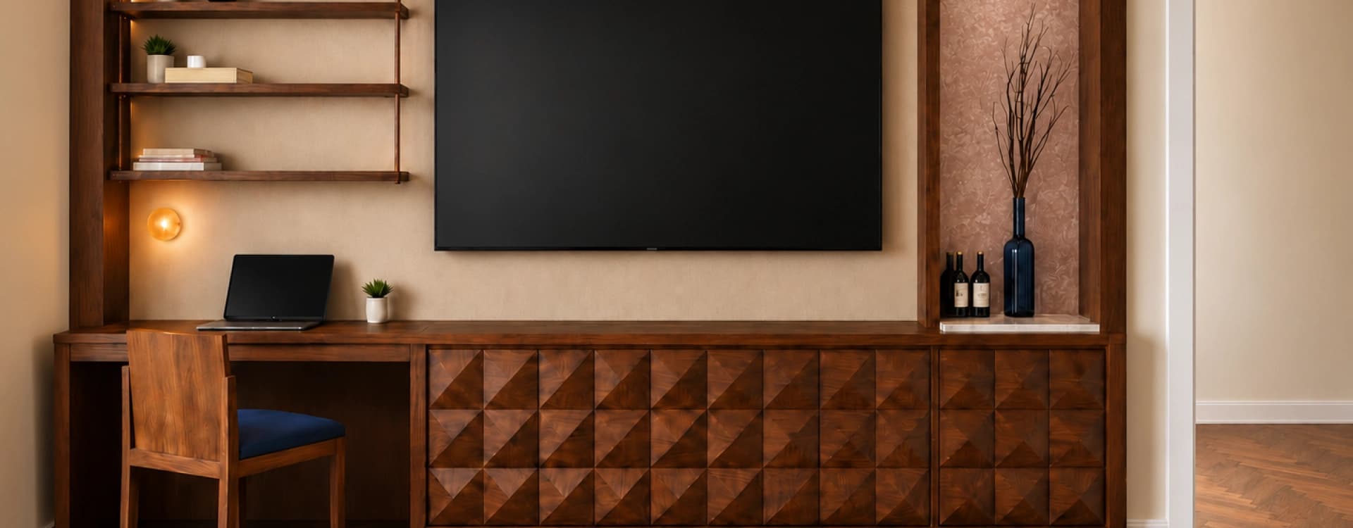 A wall-mounted television above a carved geometric wood cabinet, beside a desk and floating shelves