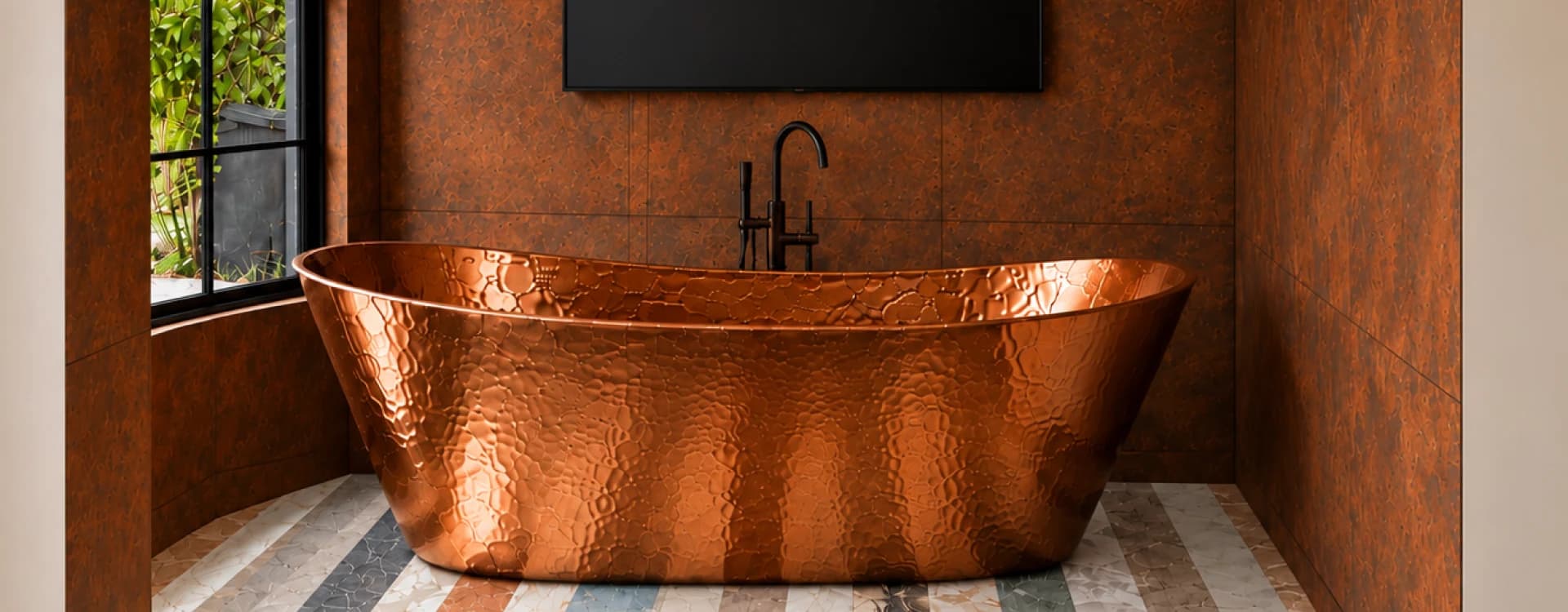 A copper bathtub facing a rust-toned wall, with a television mounted above and a window onto the garden