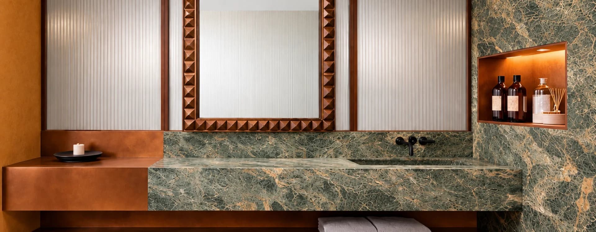 A green marble vanity beneath a hammered copper-framed mirror, beside a niche with amenities