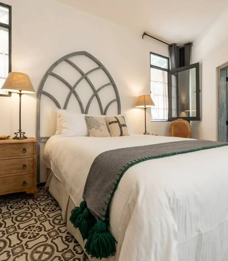 Bed with an arched cut-out headboard, a timber nightstand and a talavera mosaic floor