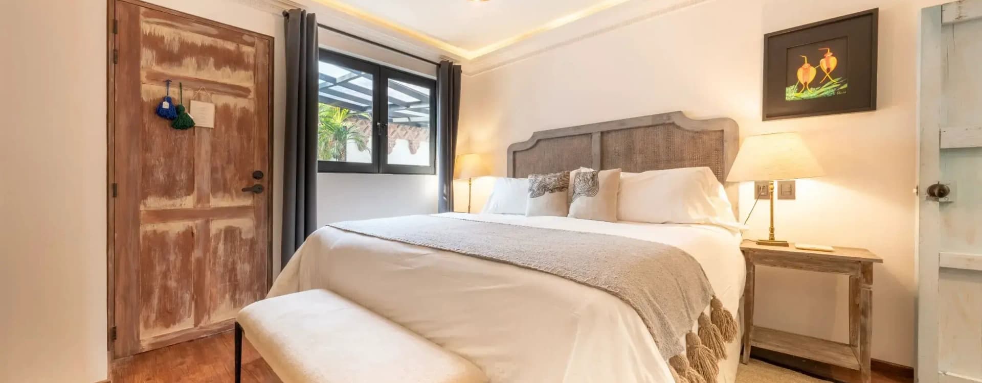 King bed with a cane headboard, an upholstered bench and a copper pendant lamp