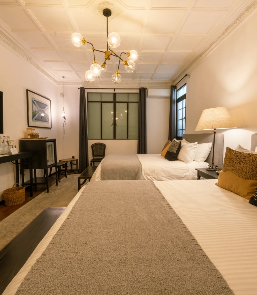 Two beds with grey wool throws beneath a coffered ceiling and a globe chandelier