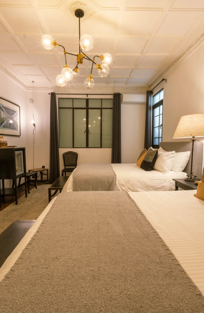 Two beds with grey wool throws beneath a coffered ceiling and a globe chandelier