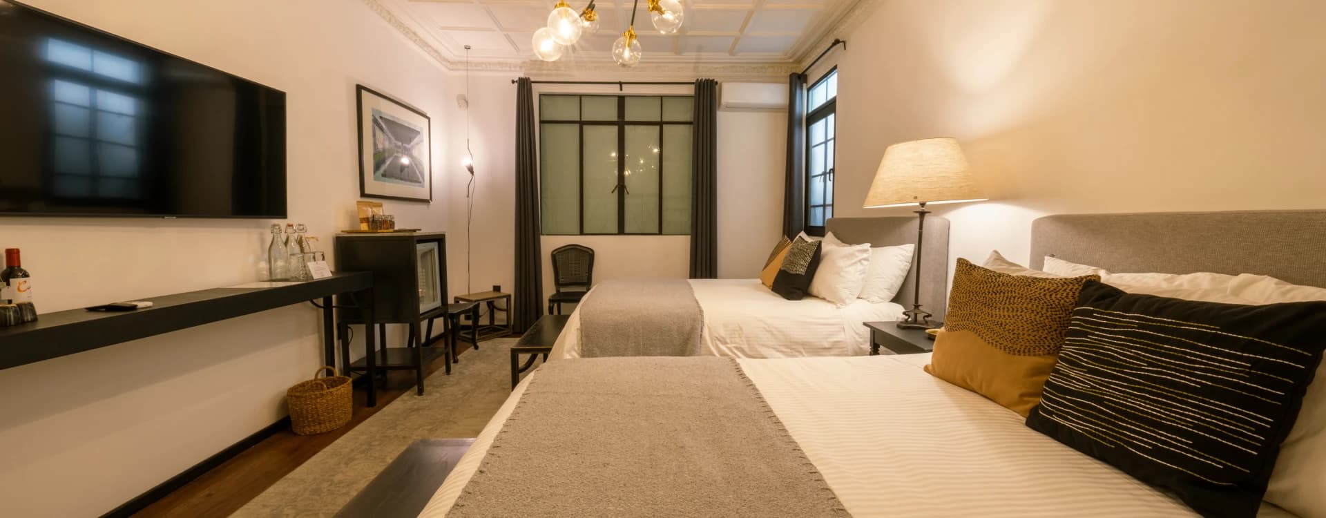 Two beds with grey wool throws beneath a coffered ceiling and a globe chandelier