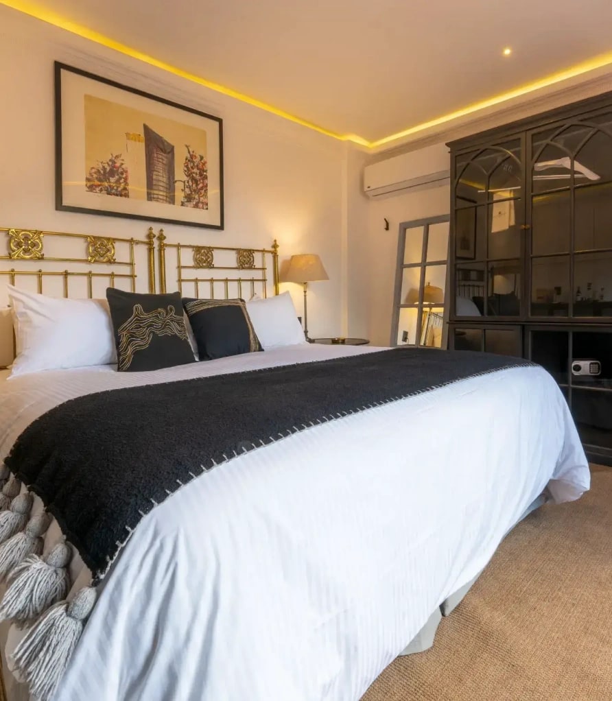 King bed with a worked brass headboard, framed artwork and a black cabinet with an in-room safe