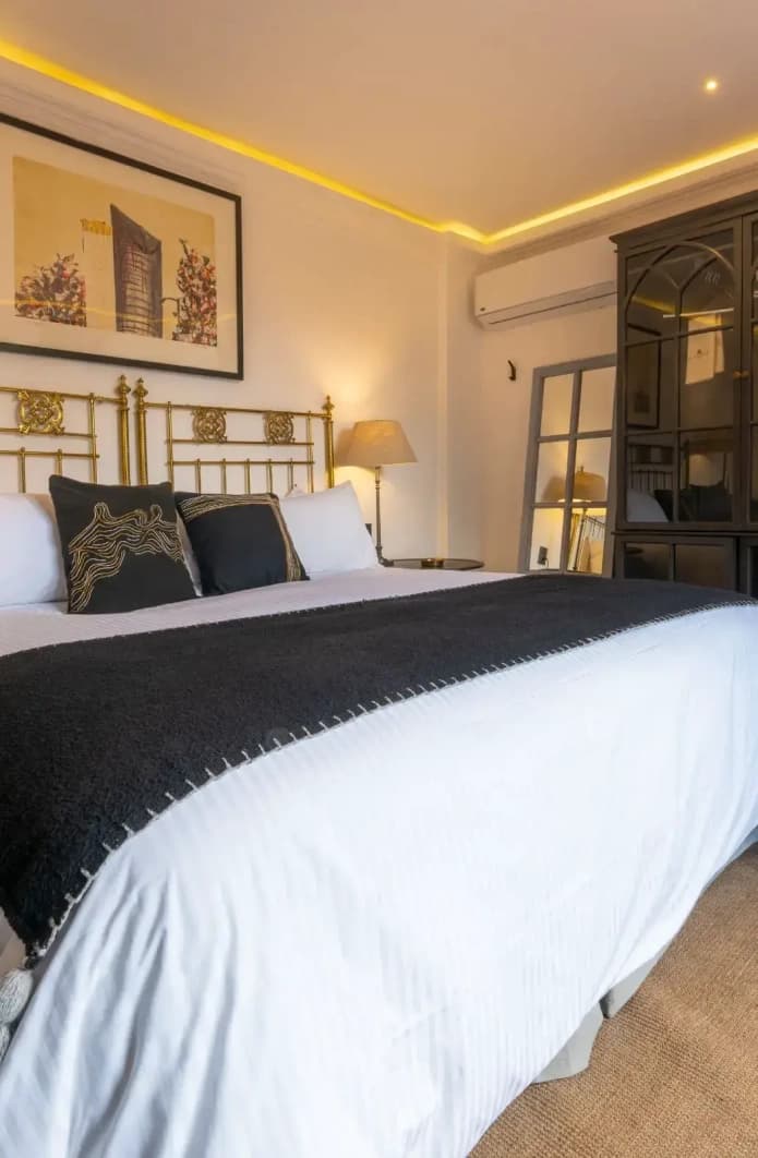 King bed with a worked brass headboard, framed artwork and a black cabinet with an in-room safe