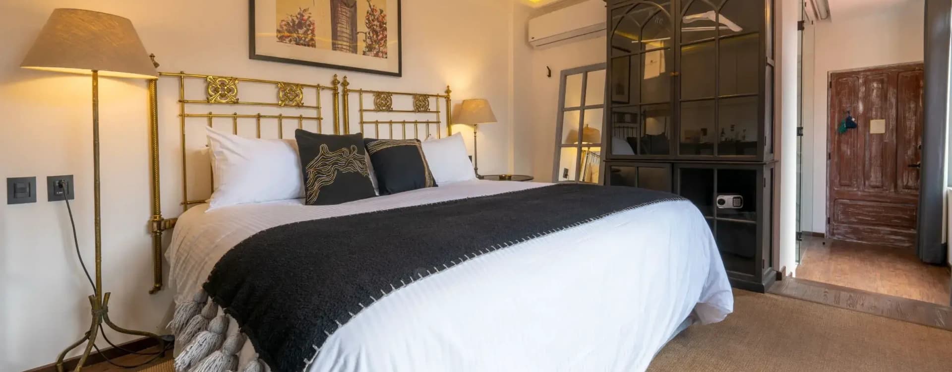 King bed with a worked brass headboard, framed artwork and a black cabinet with an in-room safe