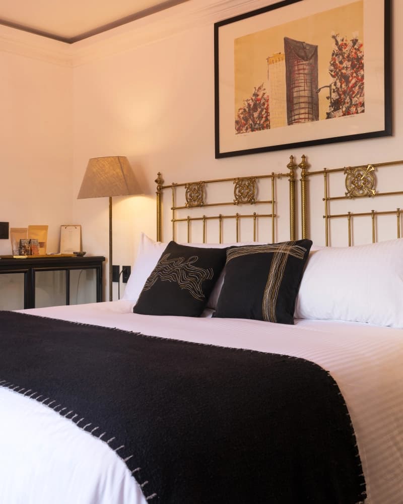 A carved brass headboard with embroidered cushions and a floor lamp beside the bed